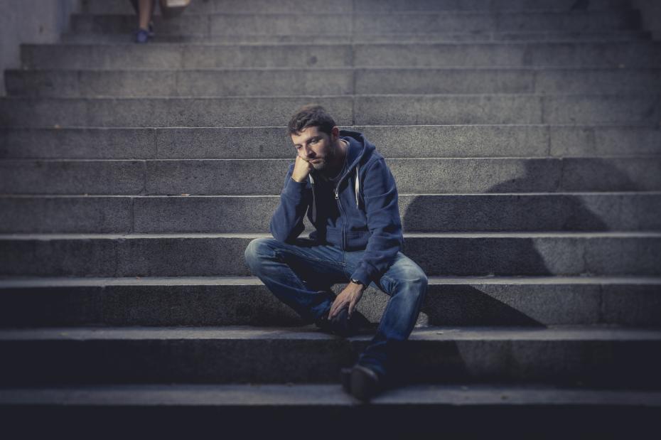 Young man lost in depression sitting on ground street concrete stairs