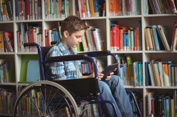 Disabled schoolboy using digital tablet in library