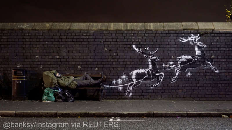 A man lays on a bench next to a new mural by Banksy in Birmingham