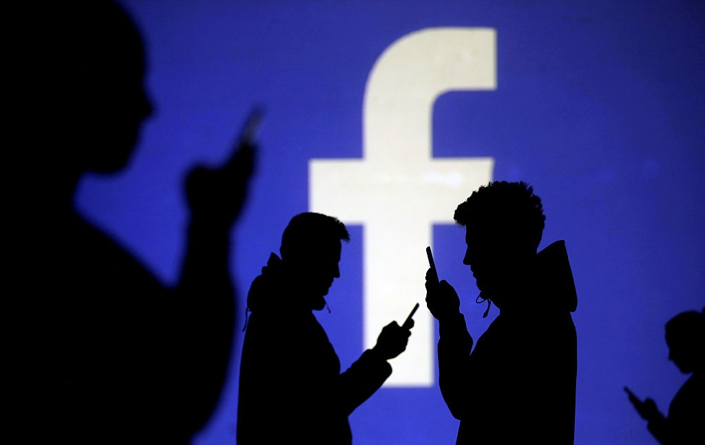 FILE PHOTO: Silhouettes of mobile users are seen next to a screen projection of Facebook logo in this picture illustration
