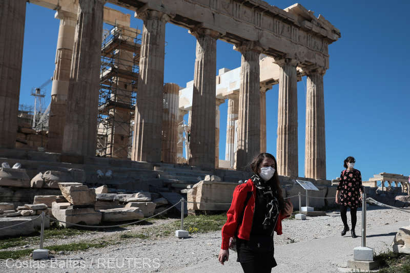 People wear protective face masks as they walk past the ancient Parthenon temple at the archaeological site of the Acropolis in Athens