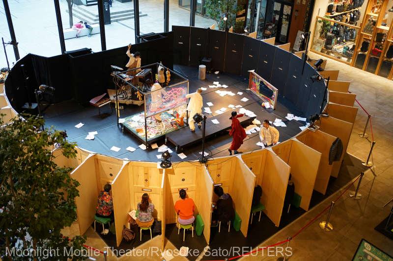 Audience members watch Moonlight Mobile Theater’s dance performance through peepholes at a shopping mall in Nagoya