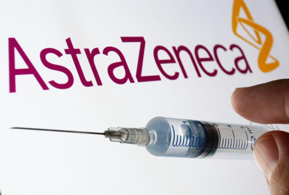 AstraZeneca Oxford vaccine concept. Syringe on a white screen and AstraZeneca logo on the blurred background.