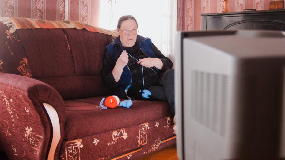 Old lady pensioner at home in glasses knitting in front of the TV