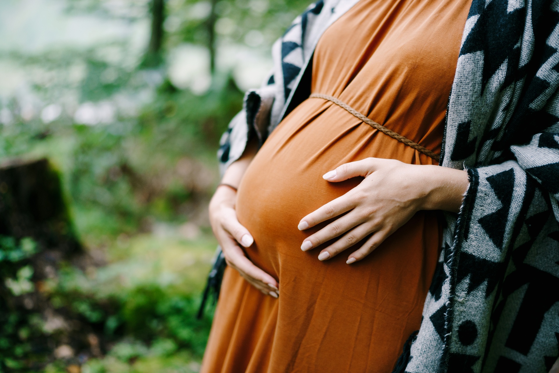 Pregnant woman hugs belly with hands in green park